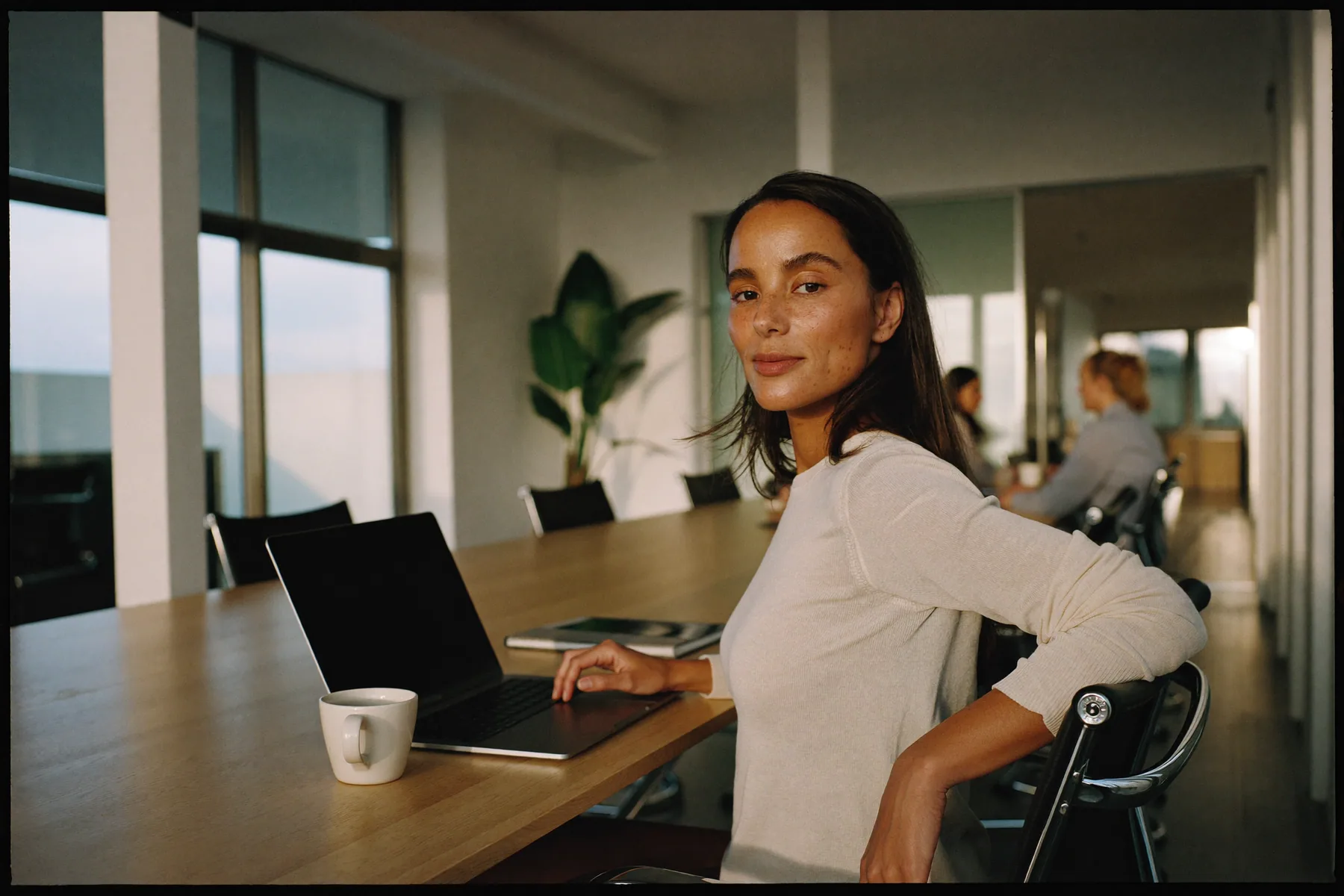 A marketing specialist at a shared desk in a bright office, turning from her laptop toward the camera